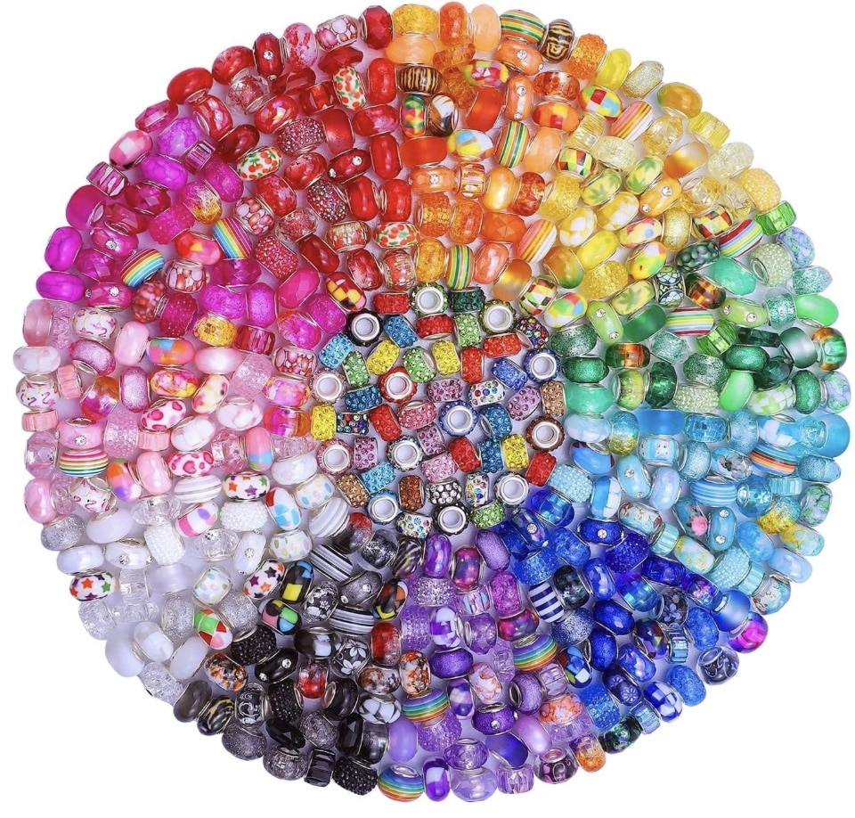 A circular arrangement of colorful glass beads, ideal for beaded garden stakes DIY, sorted by color into sections forming a gradient from red to purple, with unique patterns and designs on each bead.